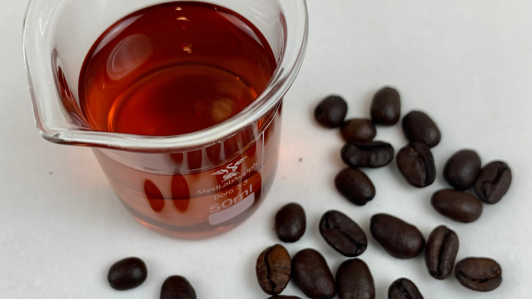 coffee seed oil in beaker with roasted coffee beans