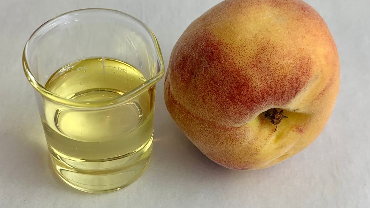 Peach Kernel Oil peach kernel oil in glass beaker with fresh whole peach fruit