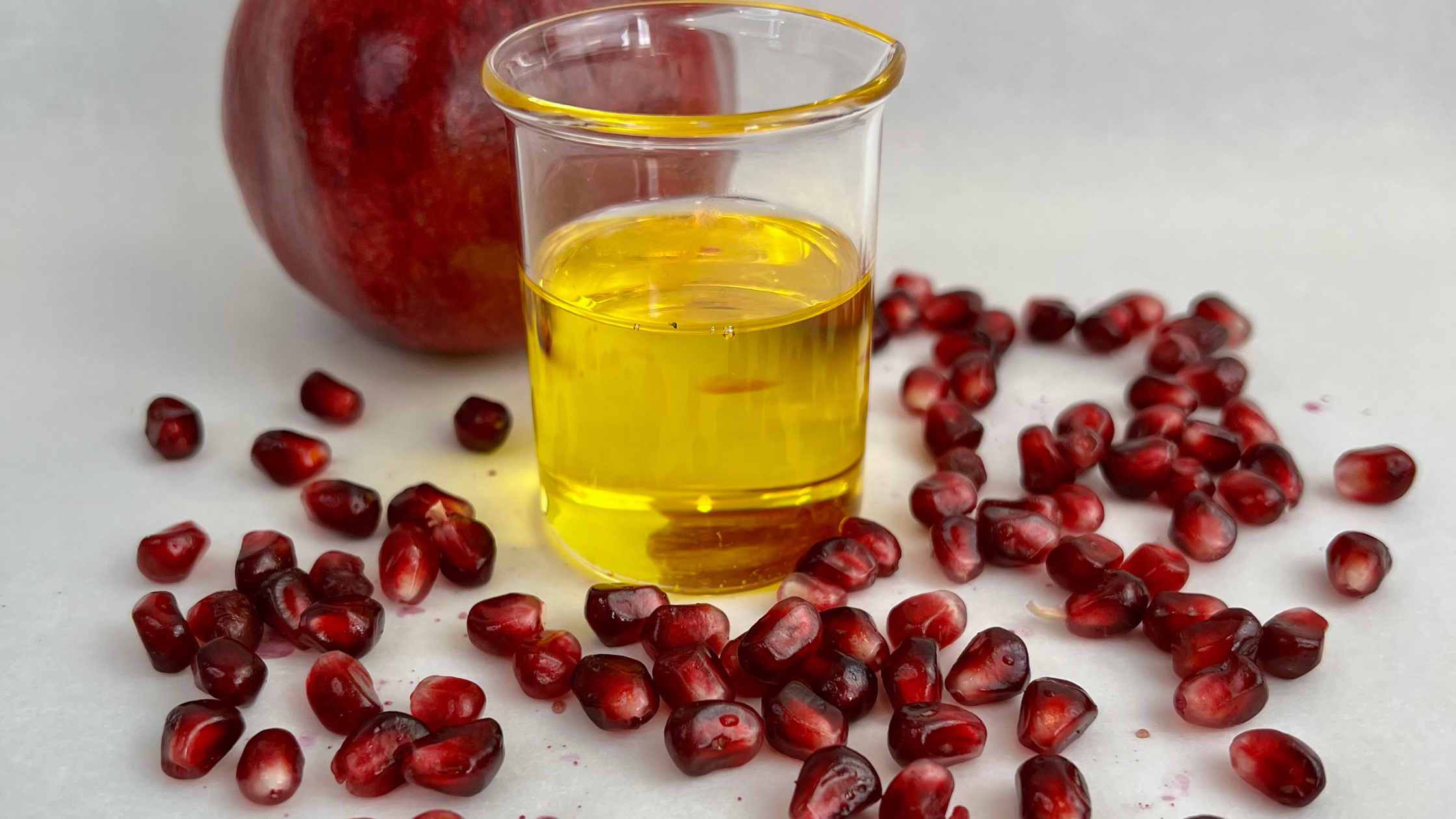 Pomegranate seed oil in beaker with fresh pomegranate seeds and fruit