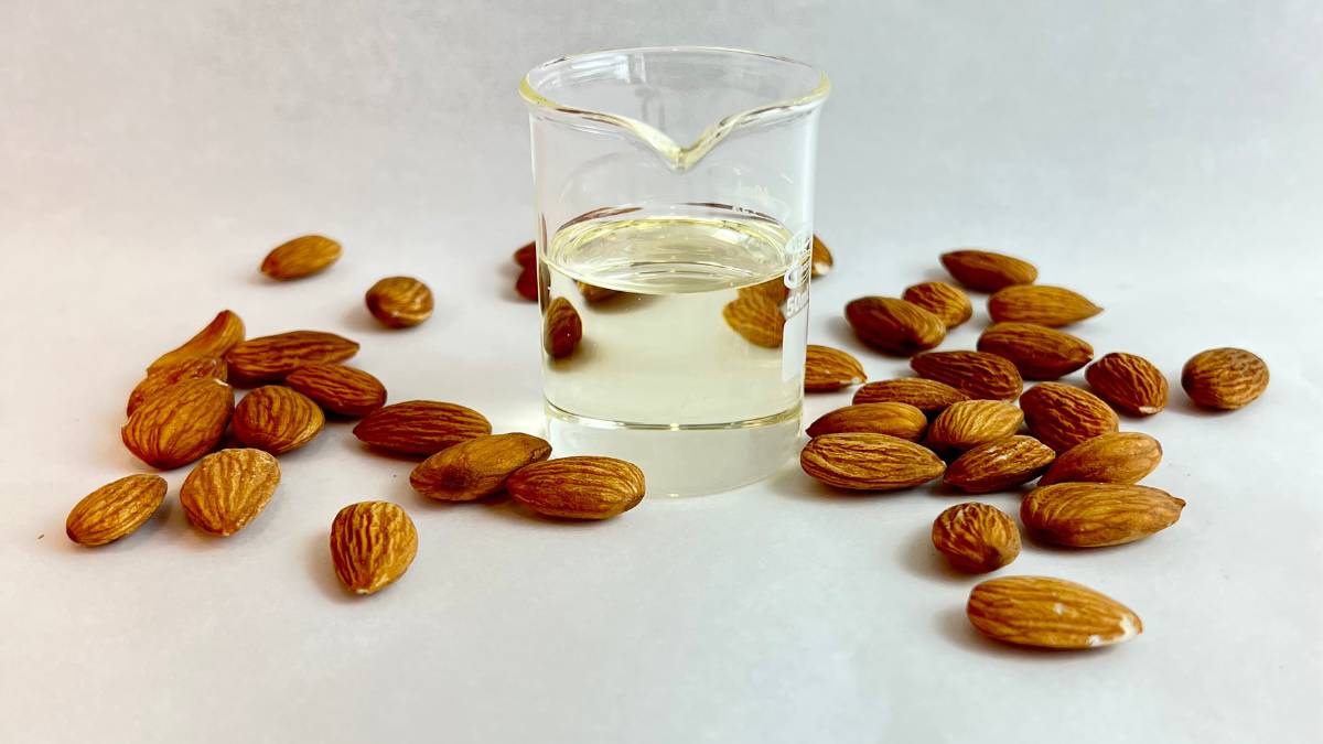 Almond Oil pale clear almond oil in glass beaker surrounded by almonds on grey background