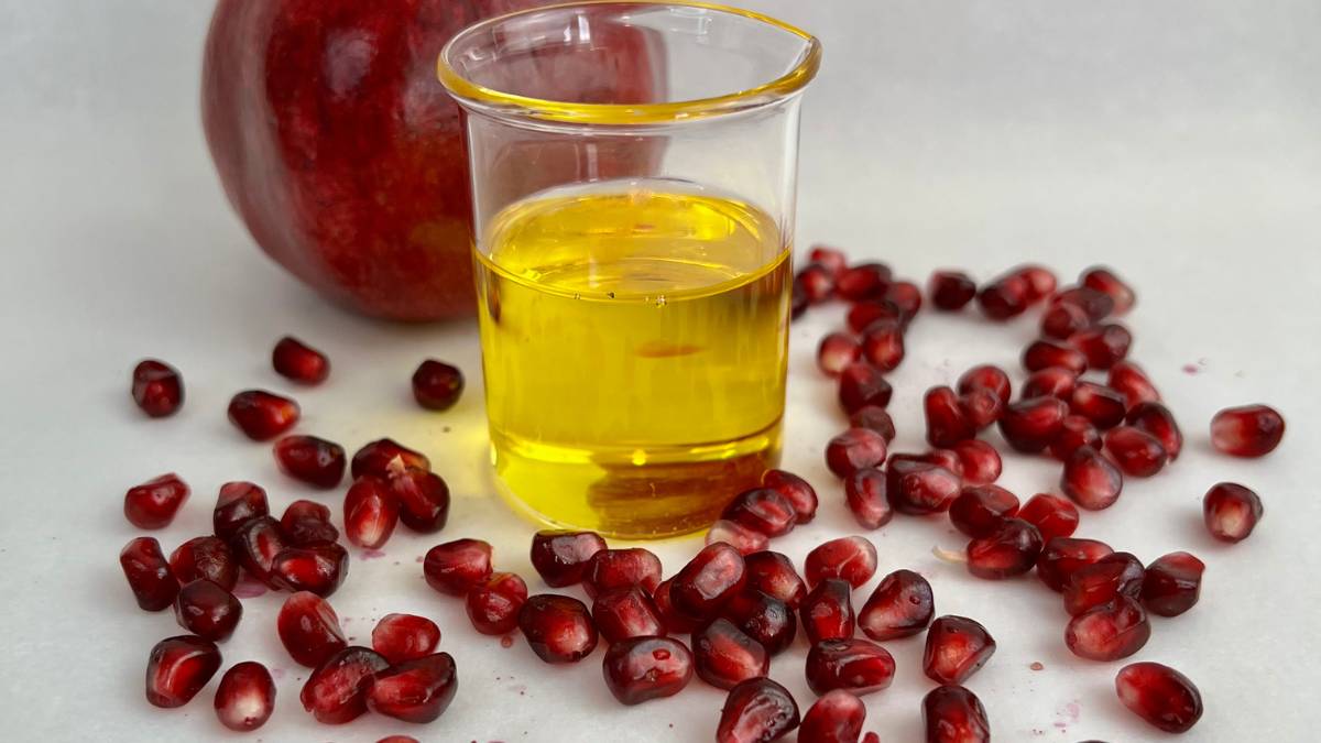 pomegranate seed oil in glass beaker with fresh pomegranate seeds scattered around it